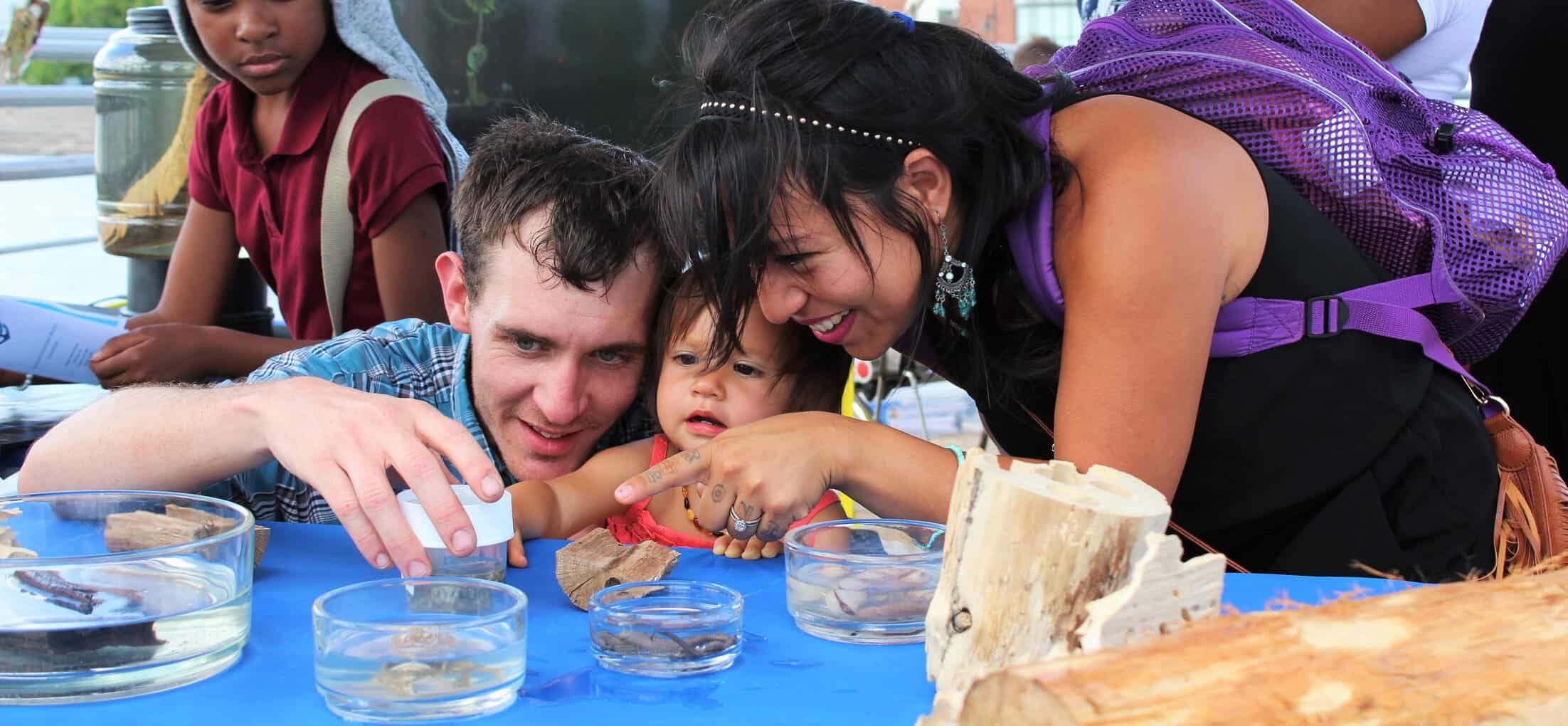 Two adults and a small child interact with items on a table