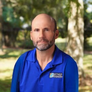 Andrew Barron in outdoor setting with trees, wearing a blue BTNEP polo shirt.
