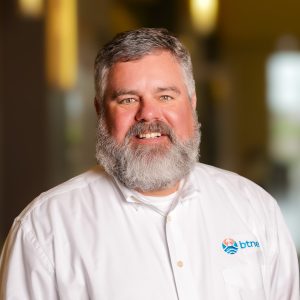 Portrait of Bren Haase with a friendly smile, wearing a white shirt with BTNE logo.