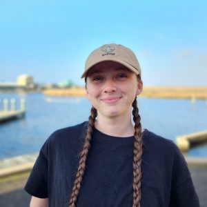 Young woman with braided hair smiling outdoors near water at LUMCON.