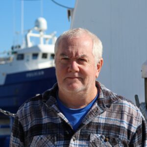 John Conover standing near a research vessel at LUMCON.