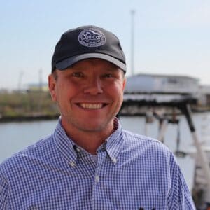 Willy Schley smiling outdoors at LUMCON with water and boats in background.