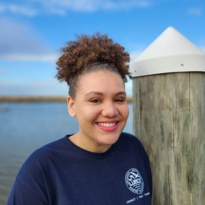 Young woman smiling outdoors near water and a wooden post.