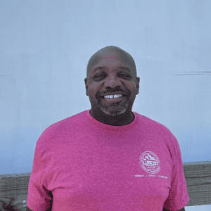 Smiling man wearing a pink LUMCON T-shirt outdoors.