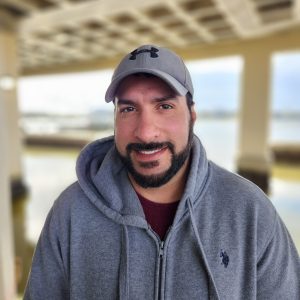 Portrait of a man wearing a gray cap and hoodie at LUMCON facility.