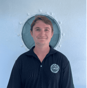 Young man in a navy polo shirt standing in front of a circular window.