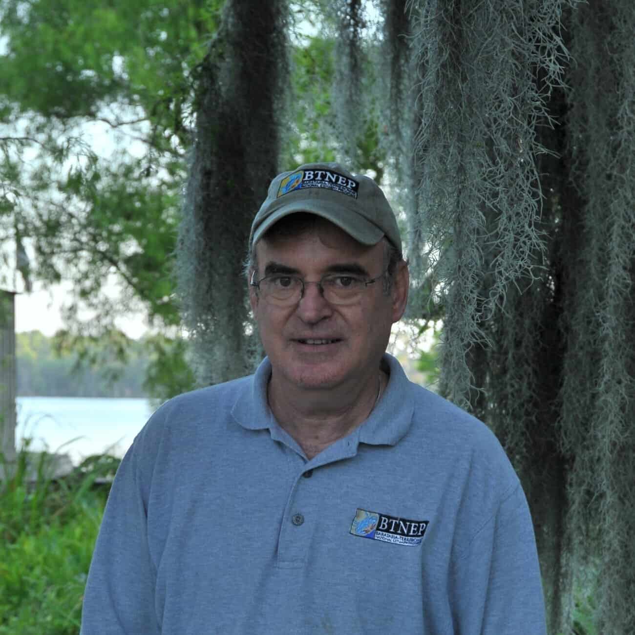 Man named Kerry St. Pe in the light blue shirt and tan cap smiling directly into camera.