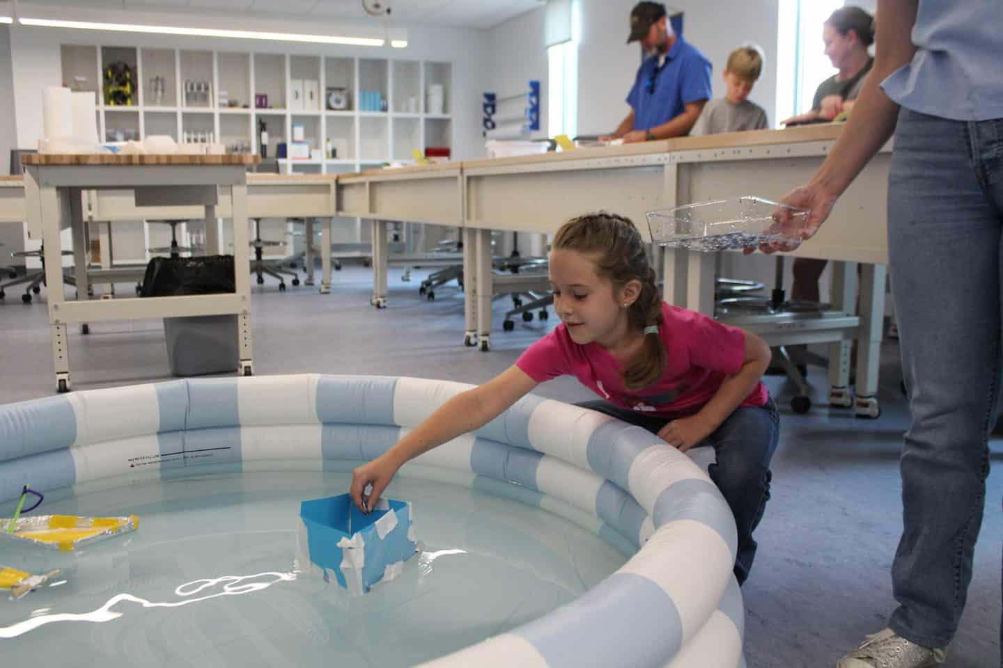 Girl puts a paper boat in a small inflatable pool